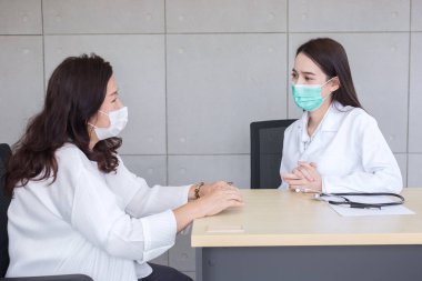 Asyalı doktor kadın hastasıyla konuşurken sağlık hizmetleri, çevre kirliliği PM2.5, yeni normal ve koronavirüs koruma kavramı hastanesinde tıbbi maske takıyor..