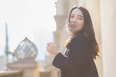 Koyu mavi takım elbiseli Asyalı güzel kız mutlu görünüyor. Güneşli bir sabahta kahve dükkanının önünde..