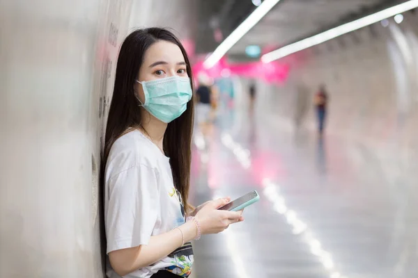 年轻的亚洲美女站在地铁隧道里 手拿智能手机 戴着口罩 这是一种新的正常和健康的生活方式 — 图库照片