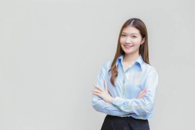 Uzun saçlı Asyalı kadın, beyaz arka planda kollarını kavuşturup gülümserken mavi gömlek giyiyor..