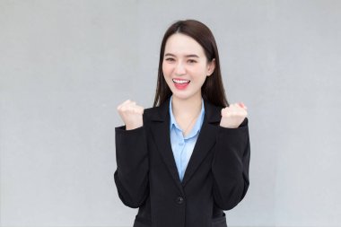 Siyah takım elbiseli Asyalı bir kadın mutlu görünüyor, gülümsüyor ve gülüyor..