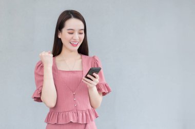 Pembe elbiseli Asyalı profesyonel çalışan kadın akıllı telefonu tutarken mutlu bir şekilde gülümsüyor..