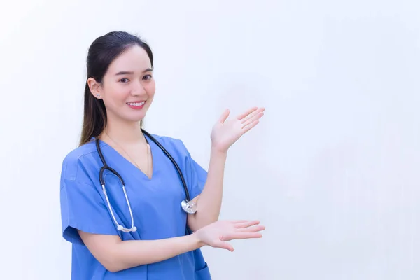 파란색 제복을 아시아의한 아름다운 의사가서 배경으로 가리키면서 미소를 짓는다 — 스톡 사진