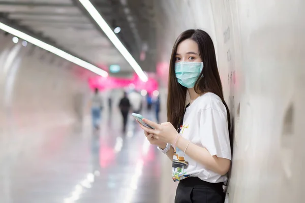 亚洲女性站在地铁隧道里 手拿智能手机 戴着口罩 这是一种新的正常和健康的生活方式 — 图库照片