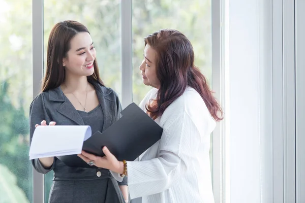 Asian business woman stands and talk to another to consult about work intently in office.