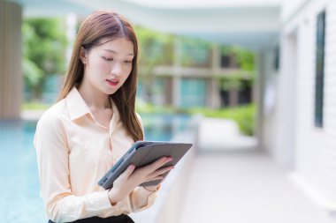 Çalışan Asyalı profesyonel genç kadın, her yerden veri aramak için tablet kullanır..