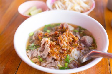 Köfte ve çorbada geniş pirinç şehriyeli et, ahşap arka planda beyaz bir kasenin üzerine turşu turşusu eklendi. Tayland 'da geleneksel Asya yemeğidir..