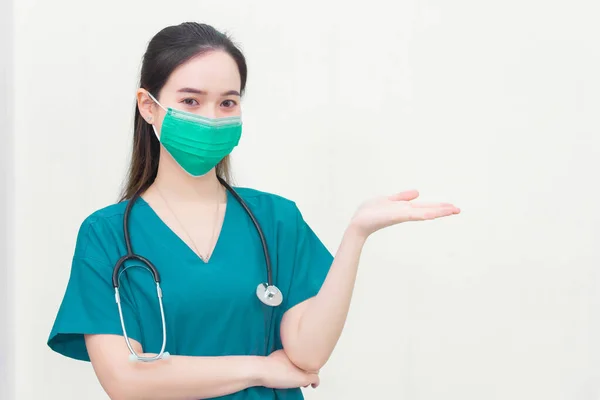 Asian woman wears green medical clothing and medical face mask to protect Coronavirus disease 2019 (Covid 19) outbreak while shows her hand to suggest something on white background.