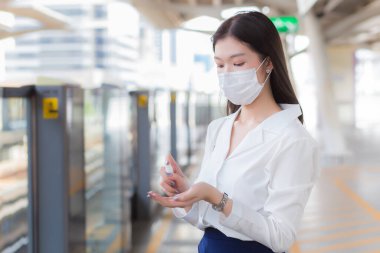 Uzun saçlı genç Asyalı iş kadını tıbbi maske takıyor ve Coronavirus 'un (COVID-19) sağlığını temizlemek ve korumak için ellerine alkol sıvısı püskürtüyor..