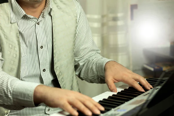 Musician's hands on the piano keyboard while playing. A man plays a synthesizer at home. Background with place for text