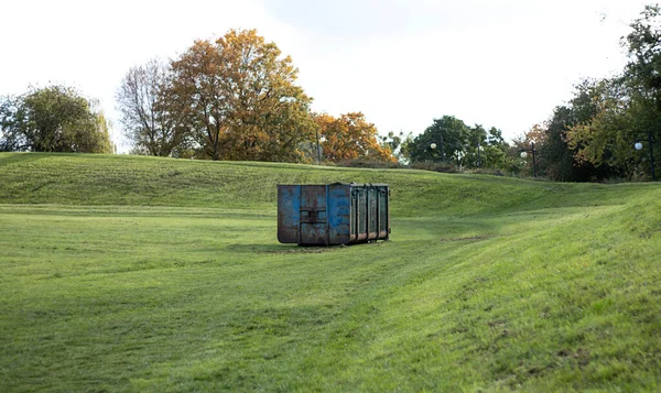 Container for collecting cut grass and fallen leaves. Large metal container for household waste. Cleaning of fallen leaves and grass. Putting order in parks and squares