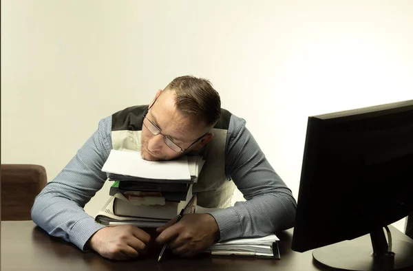 A man sleeps in the workplace on a pile of paper. Office worker sleeps on the table