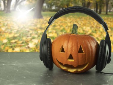 Cadılar bayramı için kulaklık takmış balkabağı ve mesaj atmak için yer. Müzisyenler için kavramsal fikir. Yüzü bir balkabağından oyulmuş. Cadılar Bayramı balkabağı kafası Sonbahar parkında Gündüz vakti sarı yaprakların arasında