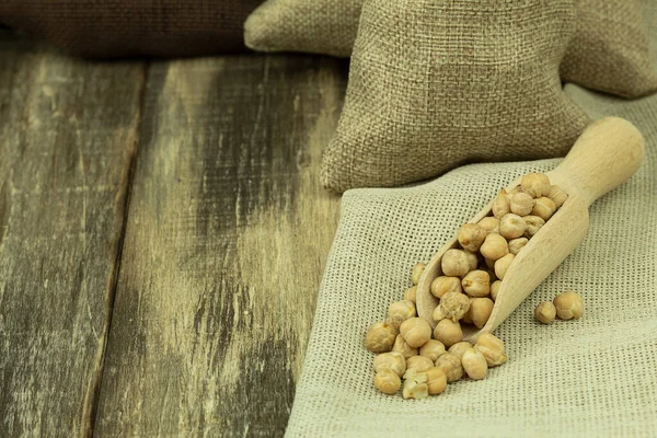 Chickpea grains in a bag on a wooden background with space for text. Chickpea seeds on a wooden spoon on sacking