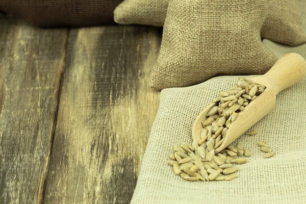 Peeled sunflower seeds in a bag on a wooden background with space for text. Peeled raw sunflower seeds with a wooden spoon on burlap