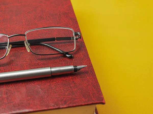 Book and glasses with a pen on the table. Background with space for text