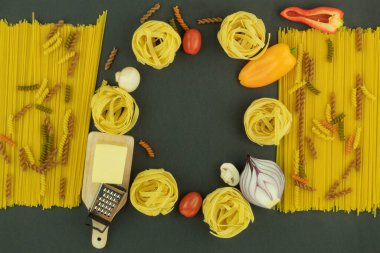 Makarna ve sebzeler arka plan olarak masanın üzerinde yazılı. Makarna arka planı. Tahta bir masada sebzeli çeşitli makarnalar. Metin için boş alan. Yukarıdan görüntüle