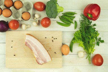 Taze tavuk yumurtası ve sebzeli pastırma. Metin için arkaplan ve boşluk. Omlet veya omlet için sebzeler masanın üzerine bırakılır. Sebze ve jambon ve domatesli çiğ yumurta.