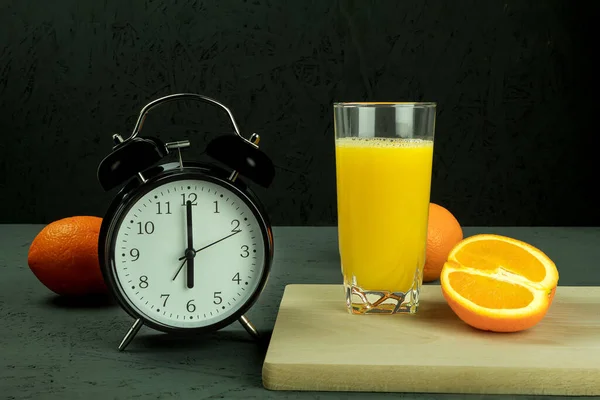 Alarm clock at which six o\'clock in the morning. Black clock and orange juice. Time - 6:00 am and Retro clock on a dark background. Copy space for text