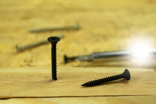 Black wood screw screwed into the board, side view macro photo. Screw for wood. Background with space for text