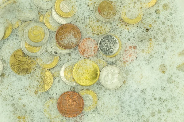 Money laundering concept, coins in soapy water. Money laundering, coins of different denominations and different countries