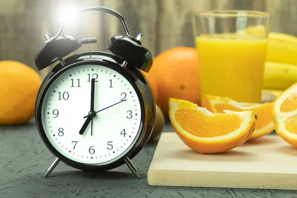 Close-up of an alarm clock with a glass of orange juice. Fresh and ripe orange and juice orange scoop on a wooden background. Organic breakfast concept