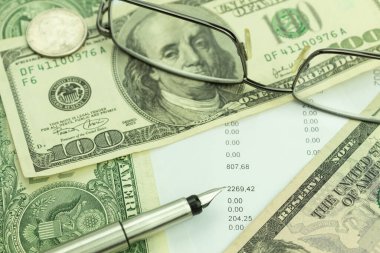 Masada dolar banknotları ve bardaklar var. Masada numaralar olan formlar. Form doldurma, vergi beyannamesi. Finansman raporu davranışları, ödemeler