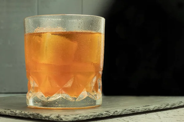 A glass with an alcoholic drink and ice. Scotch tape on a stone stand with Copyspace. Whiskey with ice. Backlit background and a glass of strong, alcoholic drink. Background with space for text