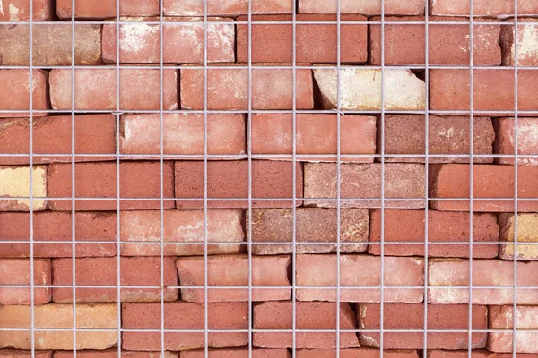 Fragment of a brick wall with a metal mesh. Texture, wall, stone texture, metal mesh, fence. Red clay stone. Clay stone wall fragment