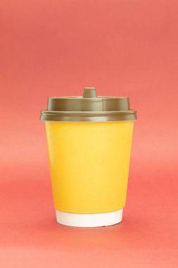 Plastik kapaklı sarı kağıt kahve fincanı. Kırmızı arkaplanda sarı cam, metin için boşluk var