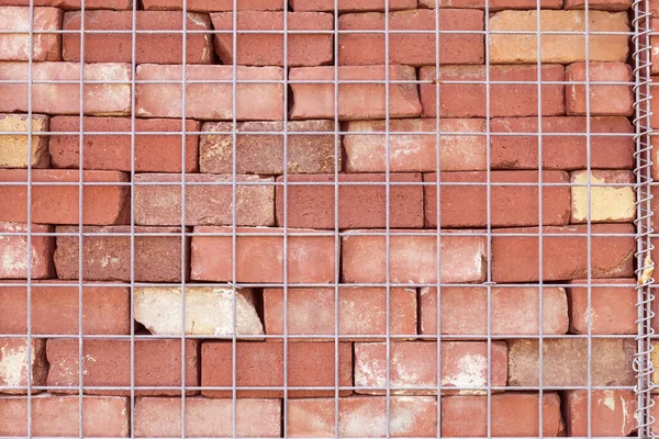 Fragment of a brick wall with a metal mesh. Texture, wall, stone texture, metal mesh, fence. Red clay stone. Clay stone wall fragment