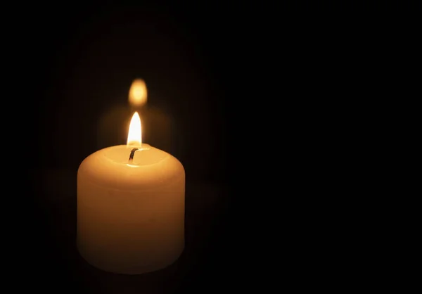Light from a wax candle burning in the dark. Candle lighting. Candle fire. Funeral fire from a candle. Fire of memory. Dark background with space for text