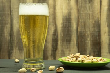 Bir bardak soğuk bira ve şam fıstığı. Bir bardak soğuk köpüklü bira, eski ahşap bir masada fındık. Metin için alanı olan arkaplan