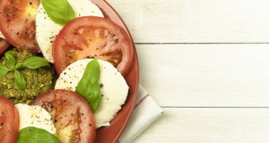 Ahşap arka planda bir tabakta Caprese salatası. Taze domates ve fesleğen yapraklı mozzarella peyniri. Ahşap bir masada salata. Kopyalama alanı olan üst görünüm