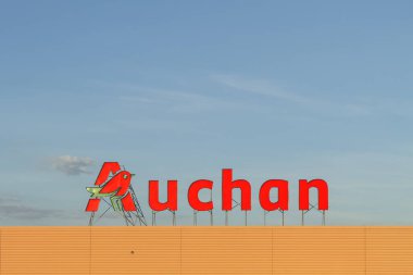 Polonya, Varşova - 2 Haziran 2021: Hipermarketin çatısında Auchan reklam tabelası. Gökyüzü arka planında Auchan süpermarket logosu