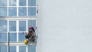 Çok katlı bir binanın camlarını temizleyen bir adam. Profesyonel pencere temizliği. Bir dağcı bir gökdelenin camını siler, alt manzara. Kopyalama alanı olan arkaplan