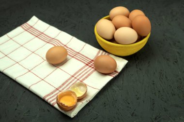 Arka planda kilden bir kasede taze tavuk yumurtası. Sarı kase ve havlunun üzerinde kahverengi yumurta. Kopyalama alanı olan arkaplan