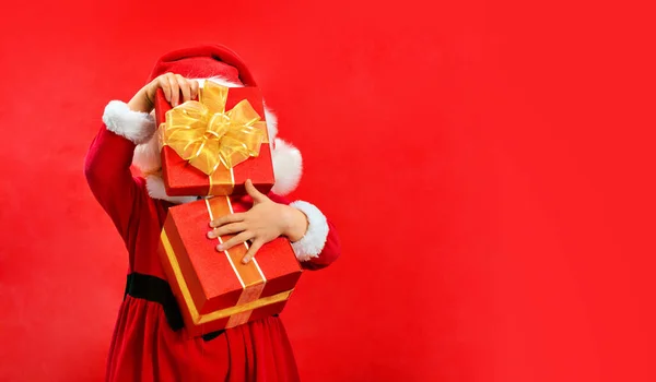 Child in Santa red hat holding Christmas gift in her hand. Christmas and new Year concept on red background. Copy space