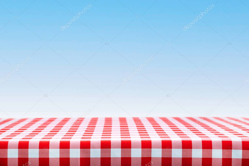 Italian cooking template - blank table with a red checked tablecloth on a blue sky background with copy space.