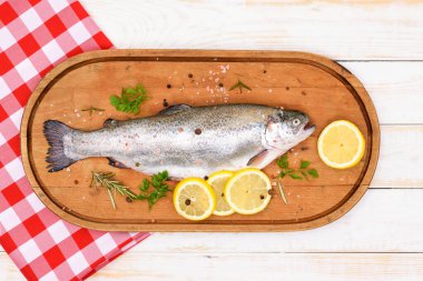 Çiğ gökkuşağı alabalığı taze otlar içinde terbiye edilmiş ve ahşap bir kesim tahtasının üzerinde pişirilmeye hazır.