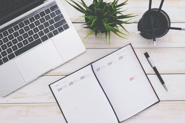 Modern iş yeri konsepti - boş bir not defteri ve odadaki ahşap bir masanın üzerindeki yeşil çiçekli gümüş bir dizüstü bilgisayarın üst görüntüsü (eski tip düşük tonlar))