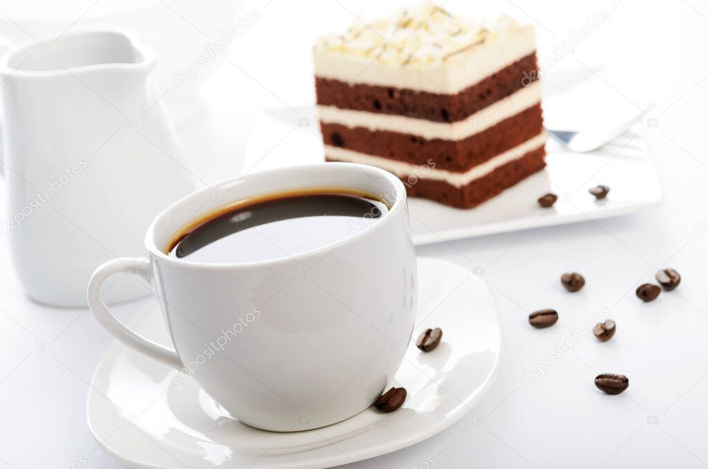 White cup of coffee with cocoa sponge cake on a saucer and scattered coffee beans in close-up