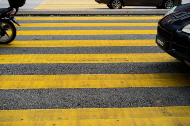 Yaya geçidinden arabalar ve motorsikletler geçiyor. Yaya geçidinin sarı çizgileri.