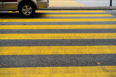 Yaya geçidinden arabalar ve motorsikletler geçiyor. Yaya geçidinin sarı çizgileri.
