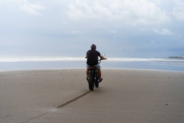Sahilde motorsiklet süren genç bir adam, açık hava portresi, güneş gözlüğü, şort, spor ayakkabı ve tişört, birlikte seyahat, okyanus, deniz...