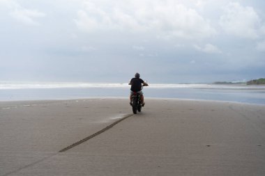 Sahilde motorsiklet süren genç bir adam, açık hava portresi, güneş gözlüğü, şort, spor ayakkabı ve tişört, birlikte seyahat, okyanus, deniz...