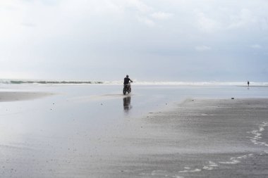 Sahilde motorsiklet süren genç bir adam, açık hava portresi, güneş gözlüğü, şort, spor ayakkabı ve tişört, birlikte seyahat, okyanus, deniz...