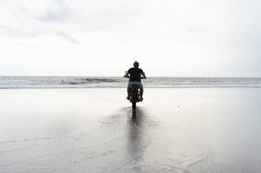 Sahilde motorsiklet süren genç bir adam, açık hava portresi, güneş gözlüğü, şort, spor ayakkabı ve tişört, birlikte seyahat, okyanus, deniz...