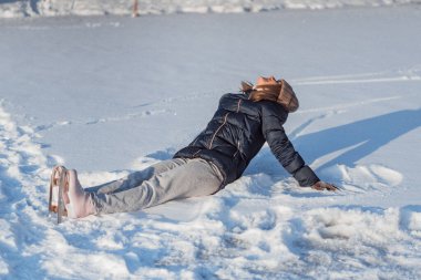 Buz pateni, genç kadın buz pateni öğreniyor, düşüyor, karda oturuyor, kış sporları, kar, kış eğlencesi.