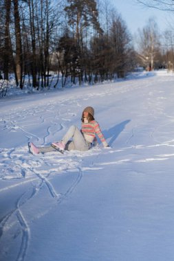 Buz pateni, genç kadın buz pateni öğreniyor, düşüyor, karda oturuyor, kış sporları, kar, kış eğlencesi.